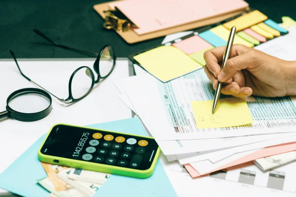 Hand writing notes while reviewing tax documents and using a calculator.