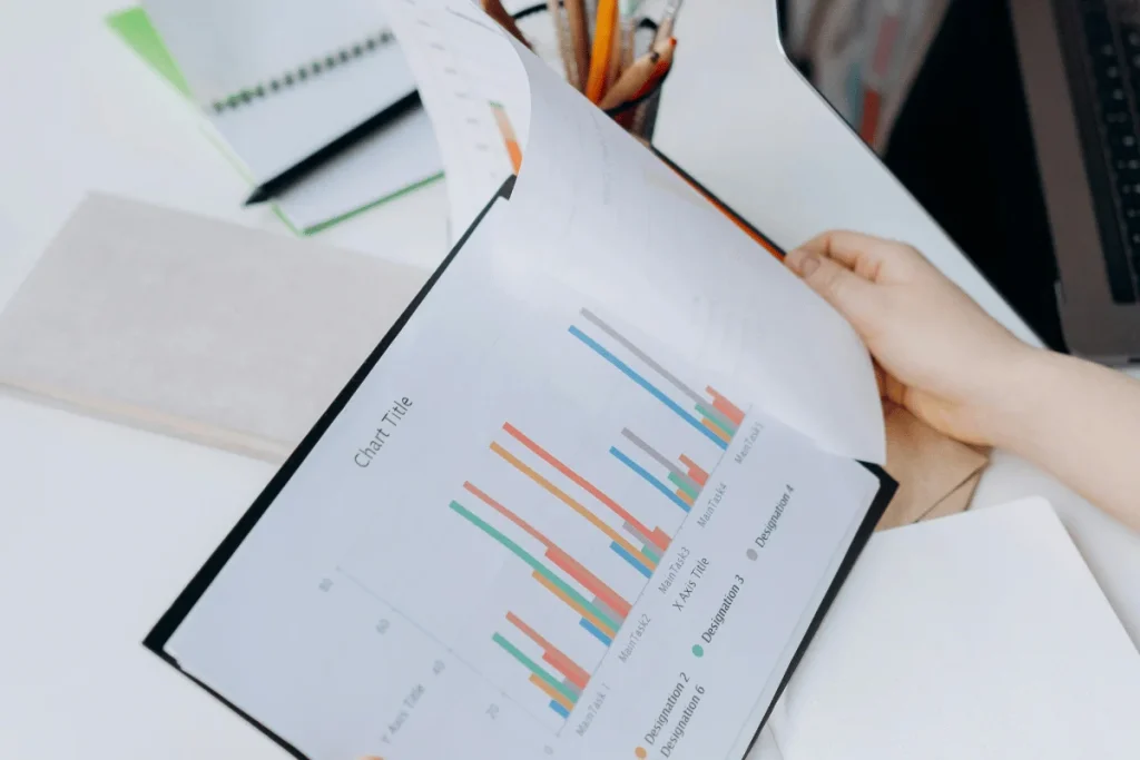 A person flips through a document featuring colorful bar charts on a desk.