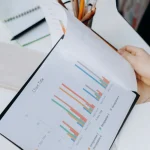 A person flips through a document featuring colorful bar charts on a desk.