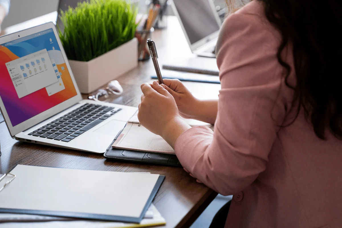 Professional taking notes at a desk with a laptop and planner.