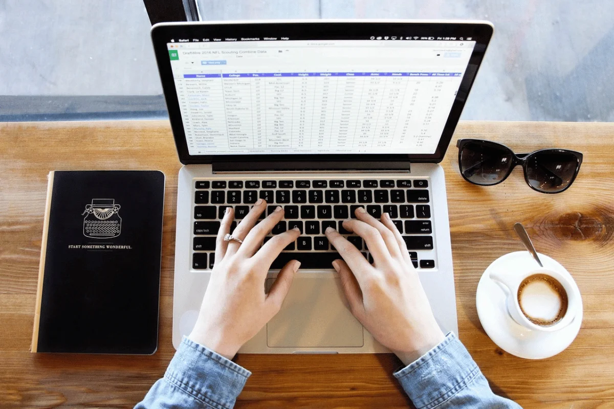 Hands type on a laptop displaying a spreadsheet.