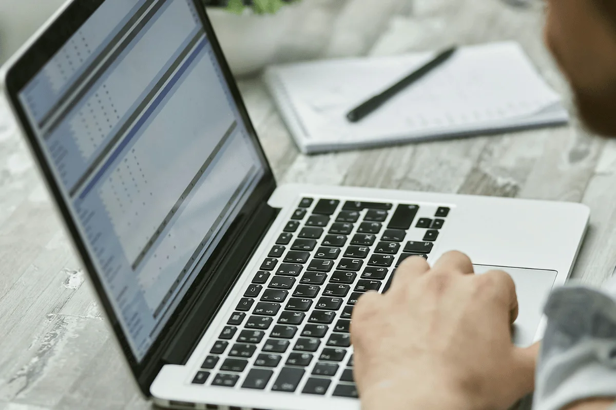 A person types on a laptop displaying spreadsheets. 