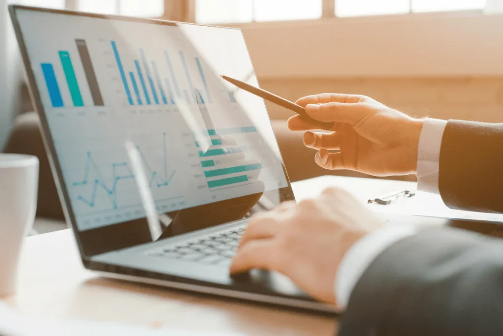 A person in a suit uses a laptop displaying bar and line charts.