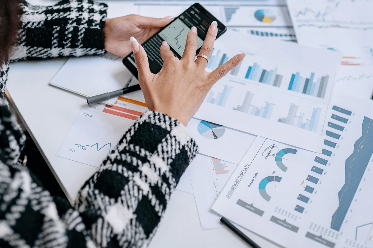 A person in a checkered coat uses a calculator-like device, surrounded by charts and graphs on a desk, conveying a focus on financial analysis.
