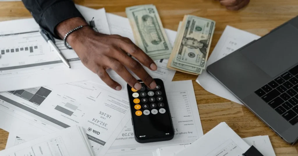 Ecommerce cash flow management workspace with calculator, dollar bills, financial documents, and laptop on wooden desk.