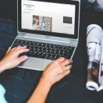 Person reviewing ecommerce marketing analytics dashboard on laptop with design materials and portfolio nearby.