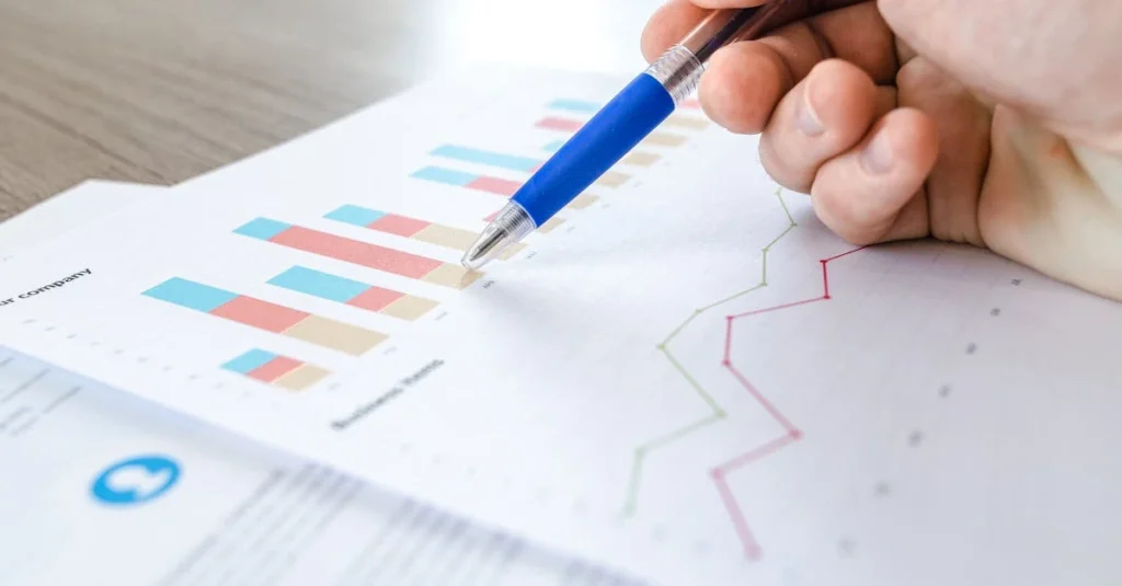 Hand pointing to bar charts and line graphs on ecommerce revenue optimization report with blue pen.