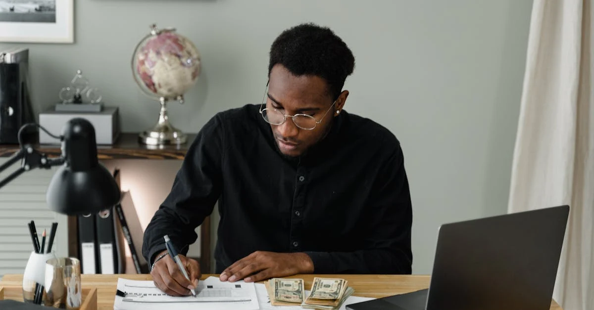 Person reviewing financial documents and spreadsheets analyzing ecommerce cash flow on wooden desk.