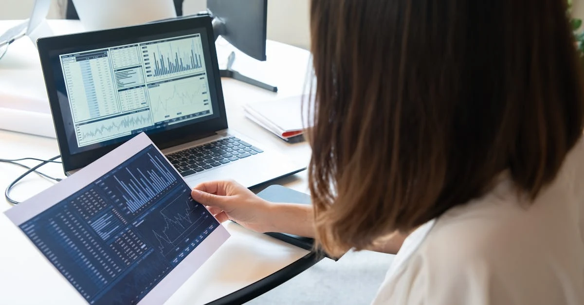 Woman analyzing ecommerce revenue optimization data on laptop and tablet at desk with multiple screens.