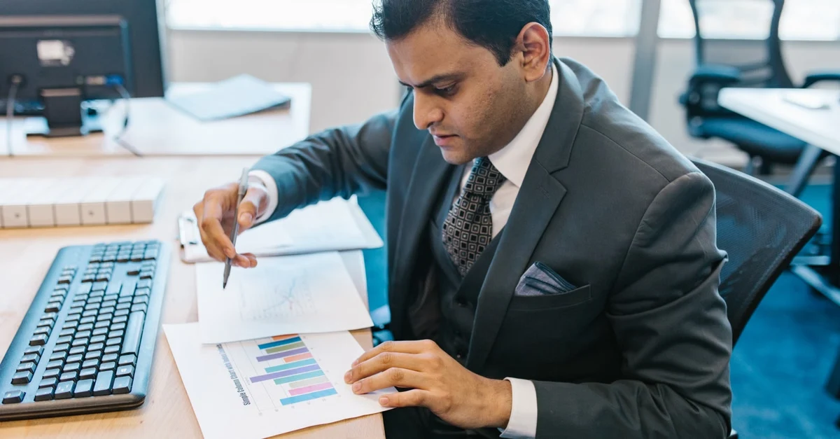 Businessman analyzing ecommerce analytics tools on printed reports at office desk with computer keyboard nearby.