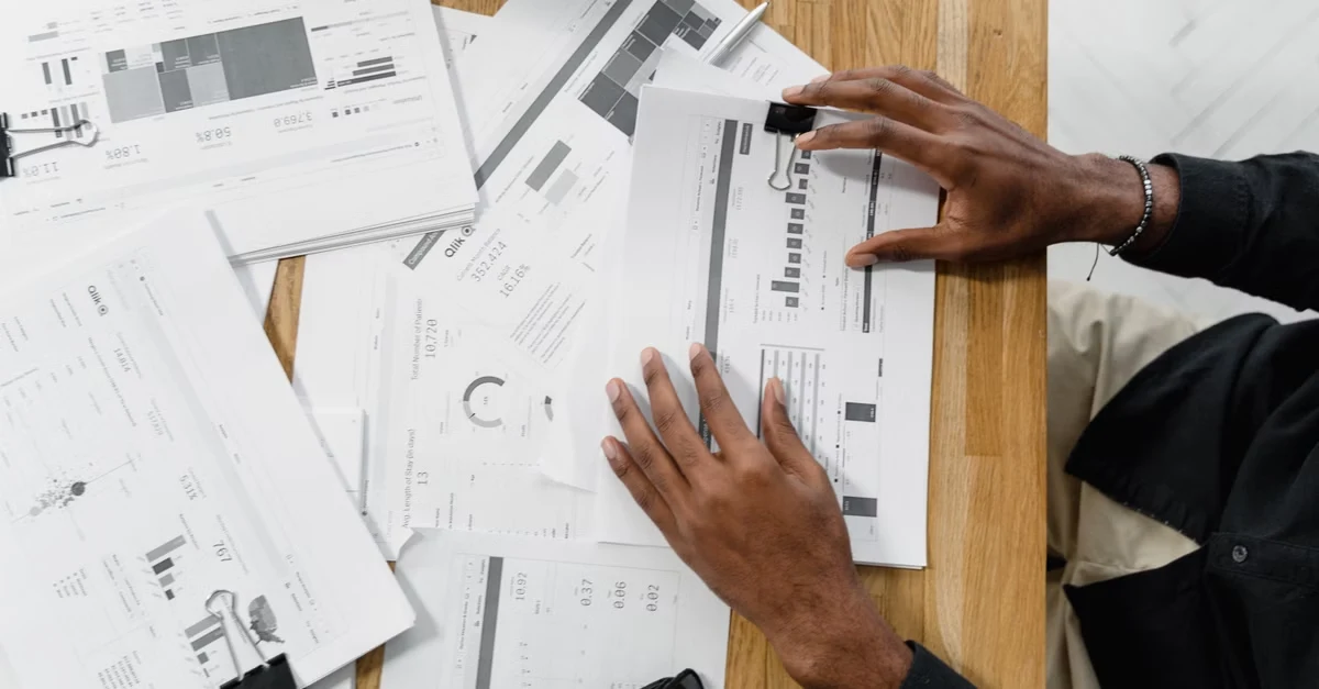Designer reviewing ecommerce marketing budget blueprints and floor plans on wooden workspace table.