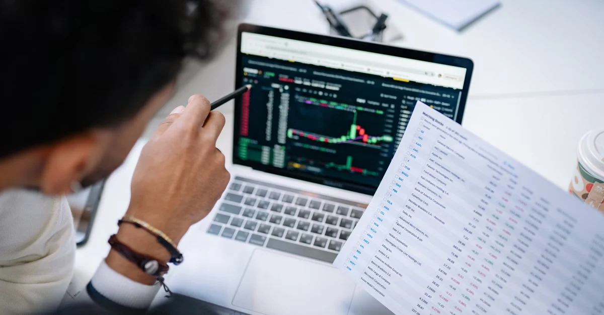 Analyst reviewing ecommerce marketing analytics charts on laptop with printed data reports on desk.